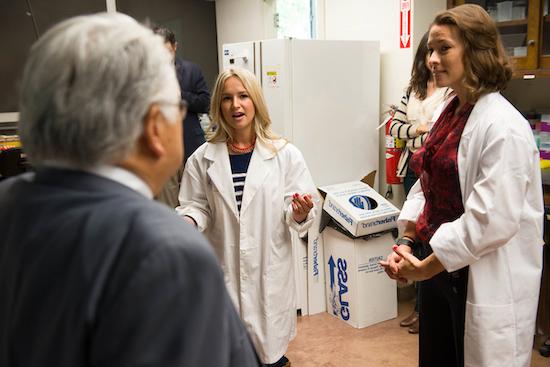 two people in lab coats talk to visitor in lab